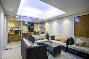 Un interior moderno con mobiliario de mimbre, una mesa de centro de vidrio y una zona de centro de negocios con computadoras y un mostrador de recepción.