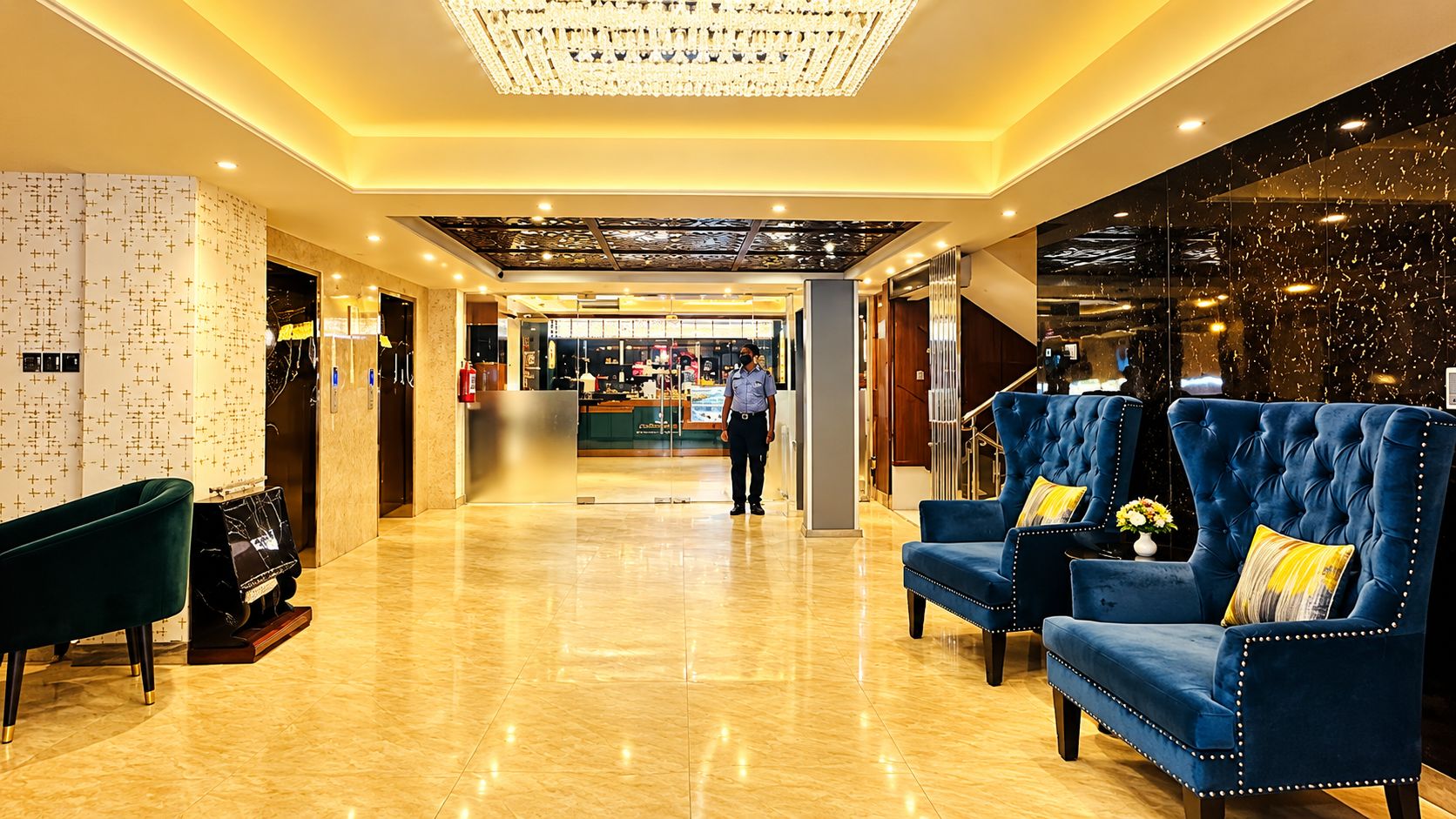 Rebedor d'hotel amb sòl de marbre, una taula de recepció i cadires blau amb coixins grocs.