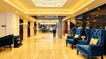 Un hall de hotel con piso de mármol, una recepción y sillones tapizados en azul con almohadones amarillos.