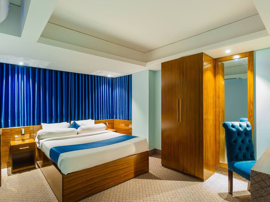 Ein Hotelzimmer mit einem hölzernen Bett, einem blauen Sessel, einem Kleiderschrank und einem Schreibtisch mit Lampe.