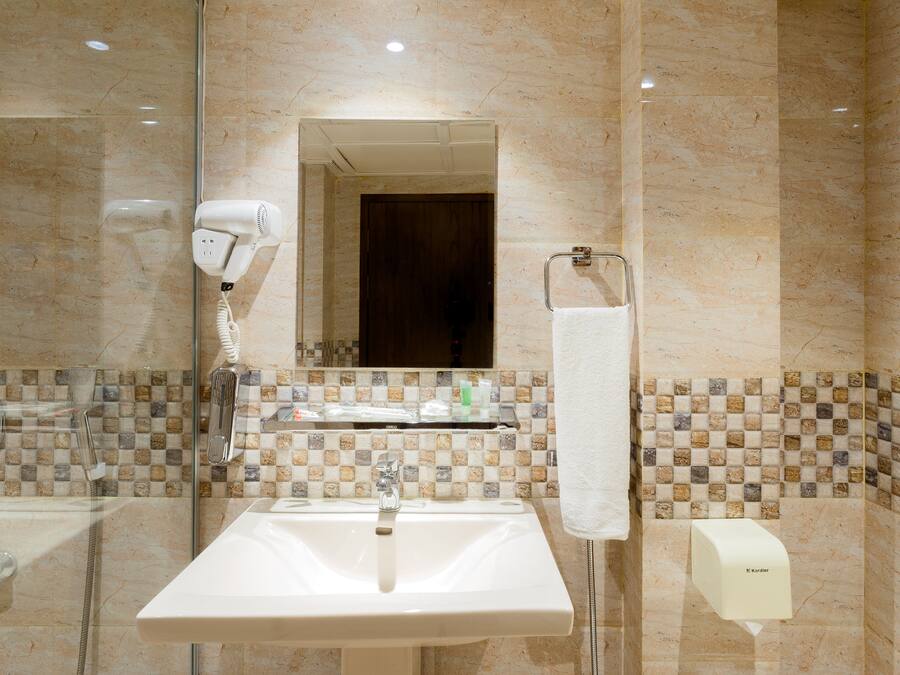 A bathroom with a sink, mirror, hairdryer, towel rack, and a soap dispenser.