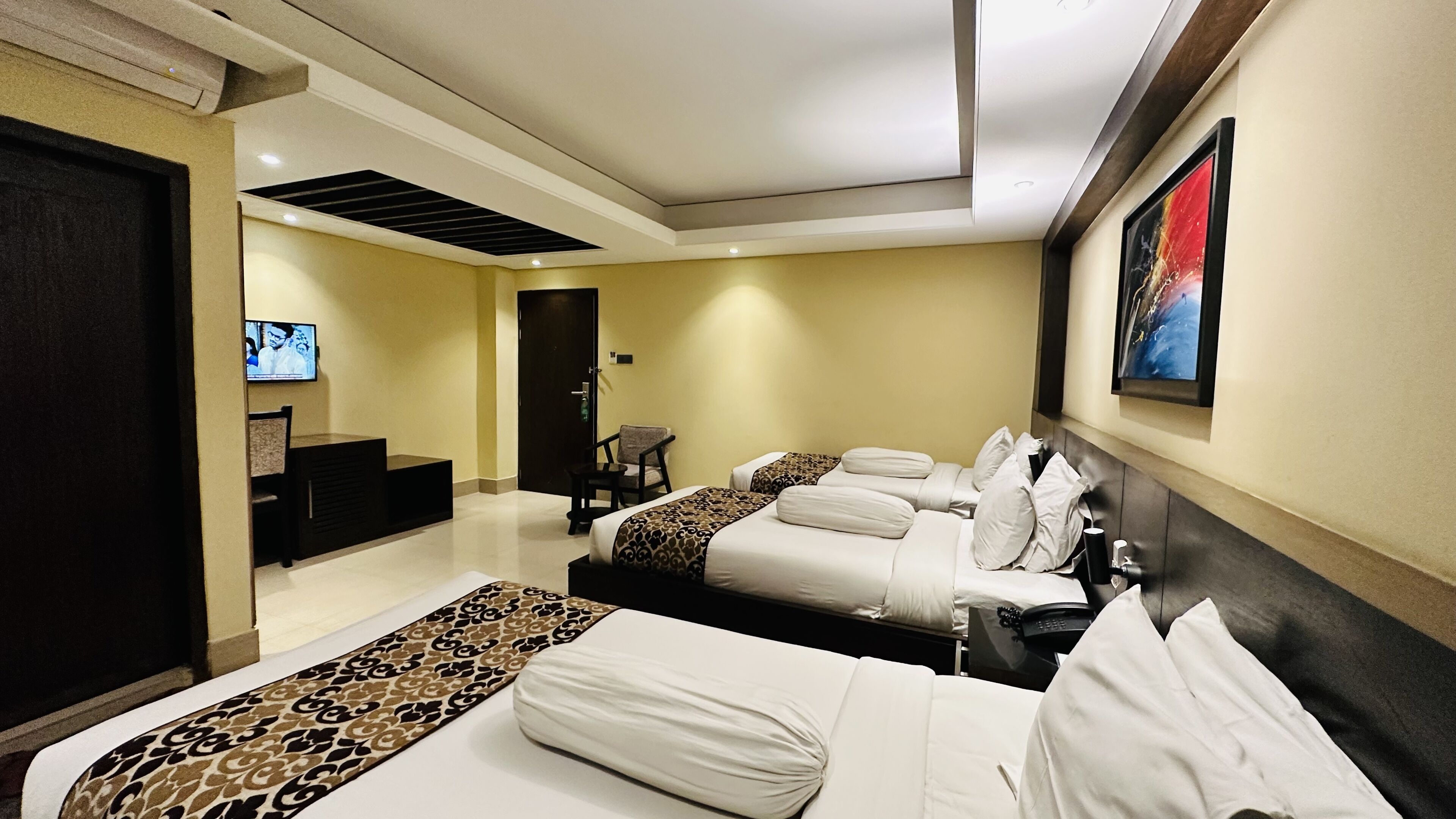 A hotel room with two beds, a desk, a chair, a TV, and a painting on the wall.