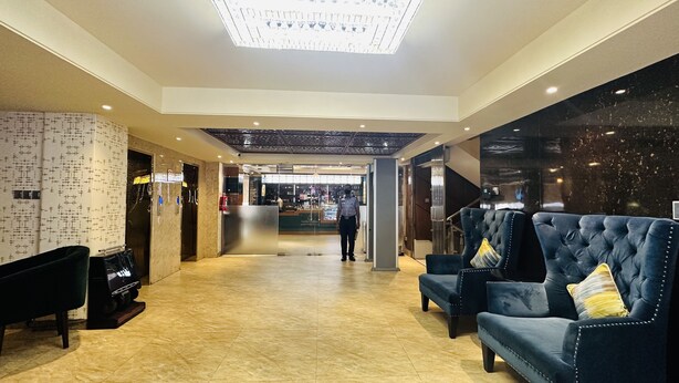 A hotel lobby with a reception desk, a security guard, and a seating area with two blue armchairs. - Hotel The Capital (Dhaka)
