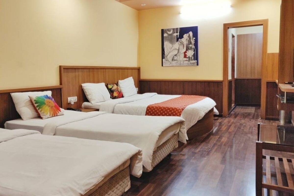 A hotel room with three beds, wooden headboards, a wooden floor, a painting on the wall, and a door to the right.