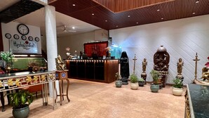 Un hall d’hôtel avec un comptoir d’accueil, des horloges, ainsi que diverses statues et plantes.
