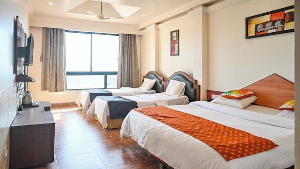 Une chambre d’hôtel avec deux lits simples, une grande fenêtre avec des rideaux, un téléviseur à écran plat fixé au mur et un plancher en bois.