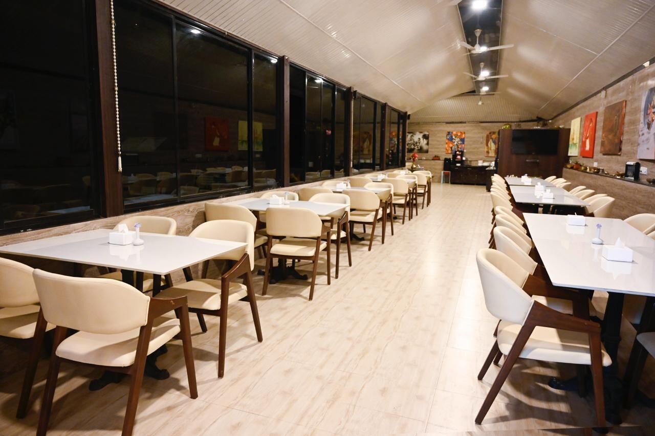 A spacious dining area with long tables and chairs, large windows, and artwork on the walls.