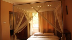 A bedroom with a four-poster bed, a window with curtains, and a wooden door. - Saltek Forest cottages (Masindi)