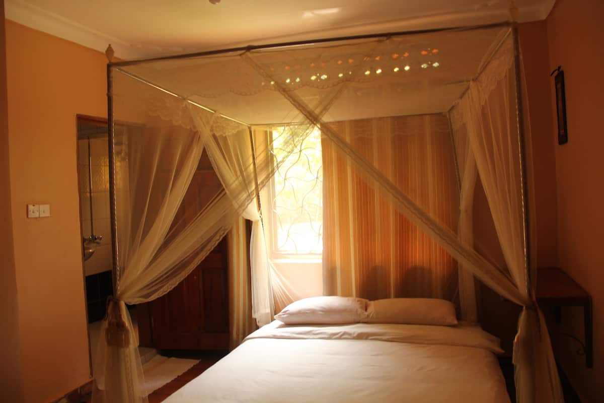 A bedroom with a four-poster bed, a window with curtains, and a wooden door.
