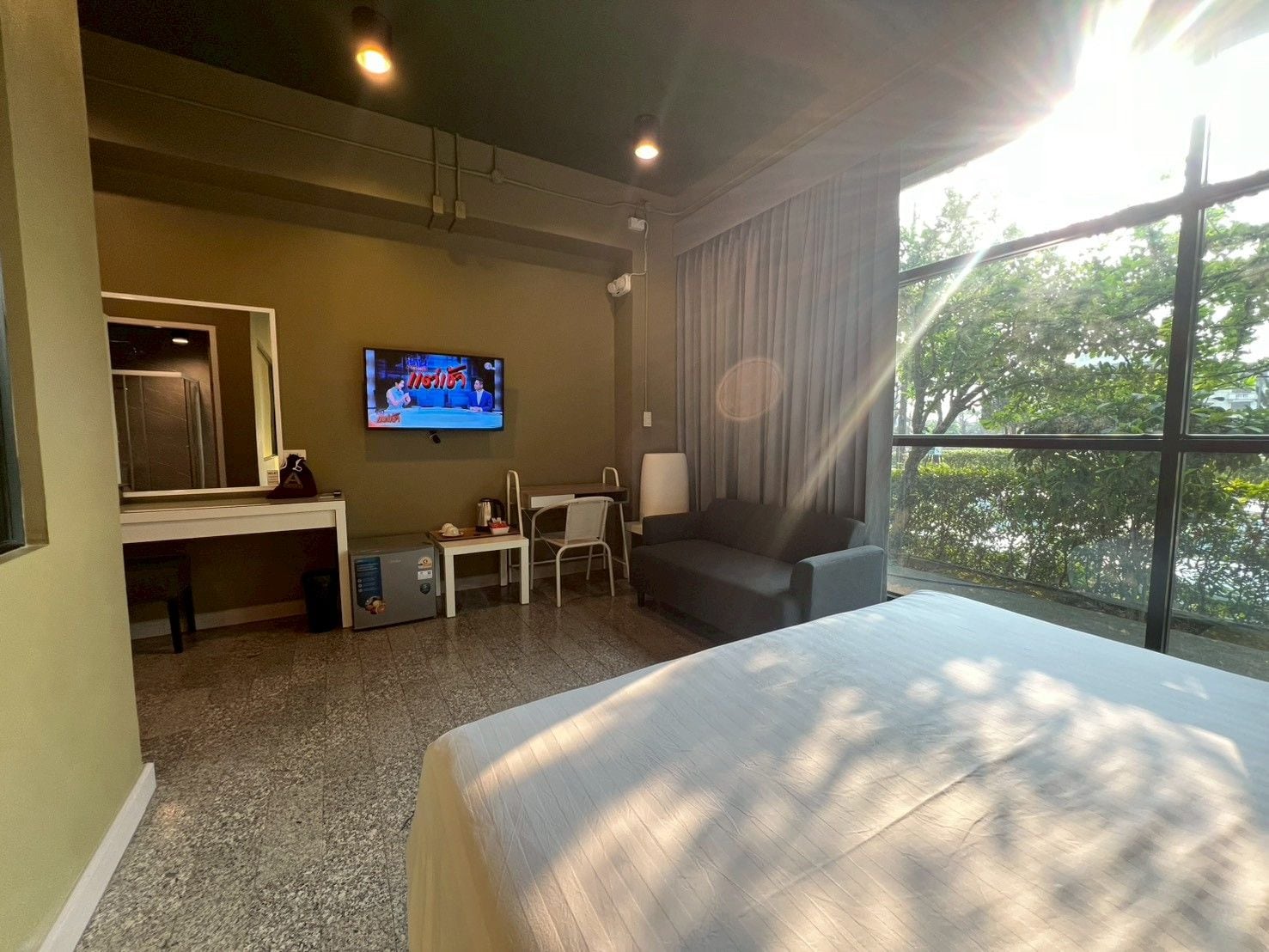 A hotel room with a bed, a desk, a TV, and a window with a view of trees.