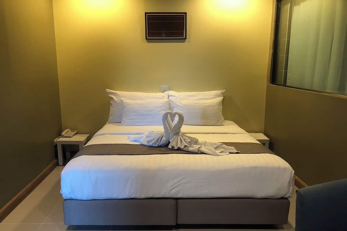 A hotel room with a bed, a bedside table with a phone, and a window with curtains.