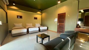 A hotel room with a large bed, two smaller beds, a sofa, a coffee table, and a wooden door.