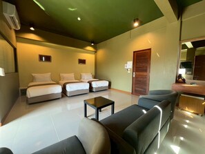 A hotel room with a large bed, two smaller beds, a sofa, a coffee table, and a wooden door.