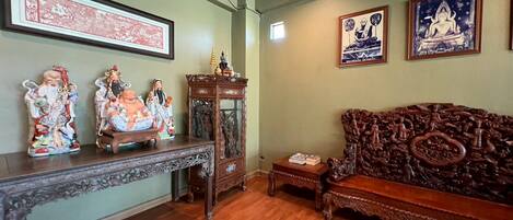 Una habitación tradicional con un sofá de madera, un aparador tallado y una pared decorada con obras enmarcadas.