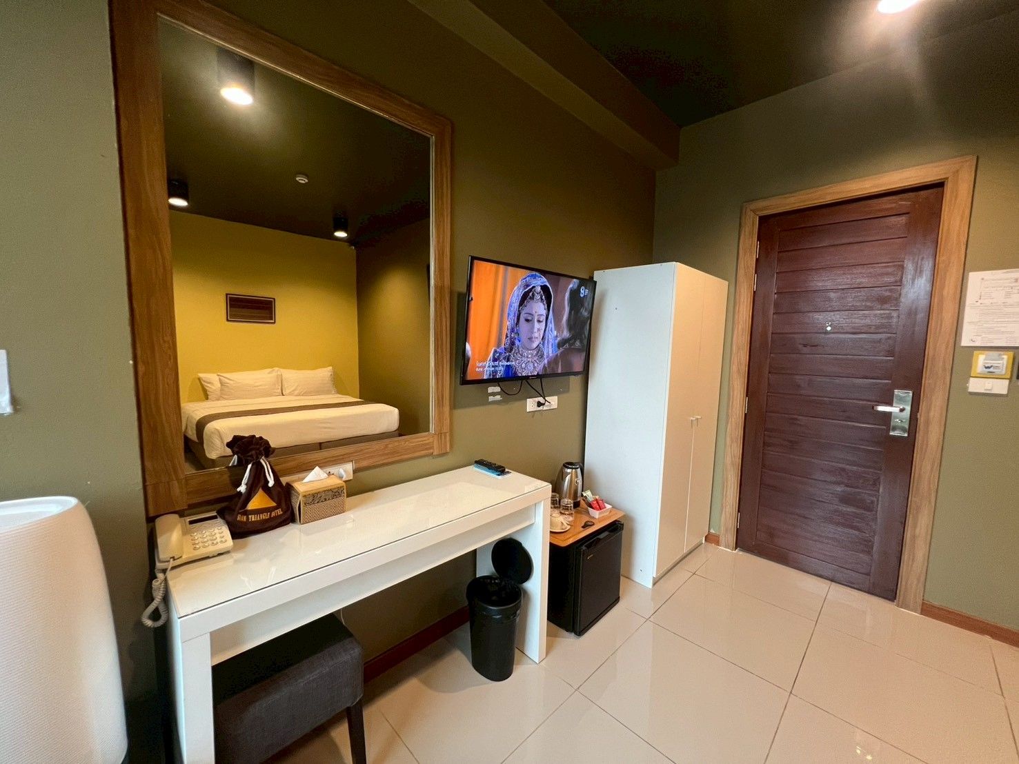 Een hotelkamer met een bed, een bureau met telefoon, een televisie, een koelkast en een deur.