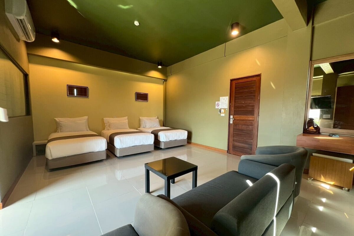 A hotel room with a large bed, two smaller beds, a sofa, a coffee table, and a wooden door.