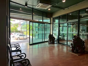 A hotel lobby with large glass doors, a wooden floor, and two decorative statues. - Work Den Chiangrai (Chiang Rai)