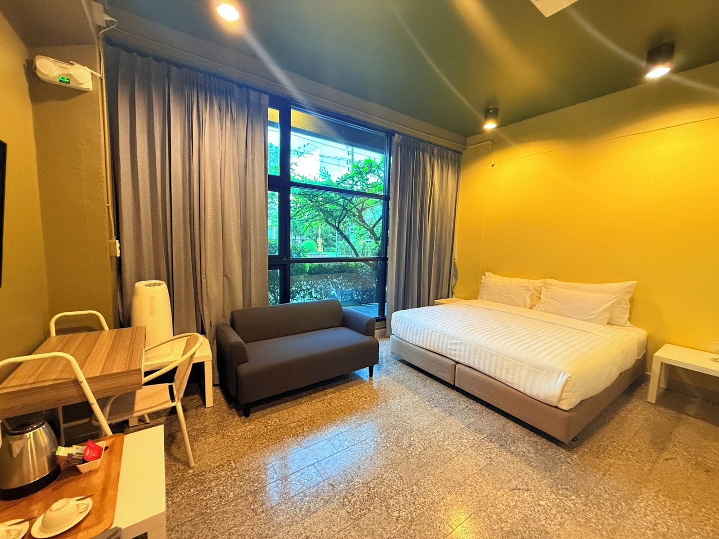 Une chambre d’hôtel avec un lit, un canapé, un bureau avec une bouilloire et une fenêtre avec des rideaux.