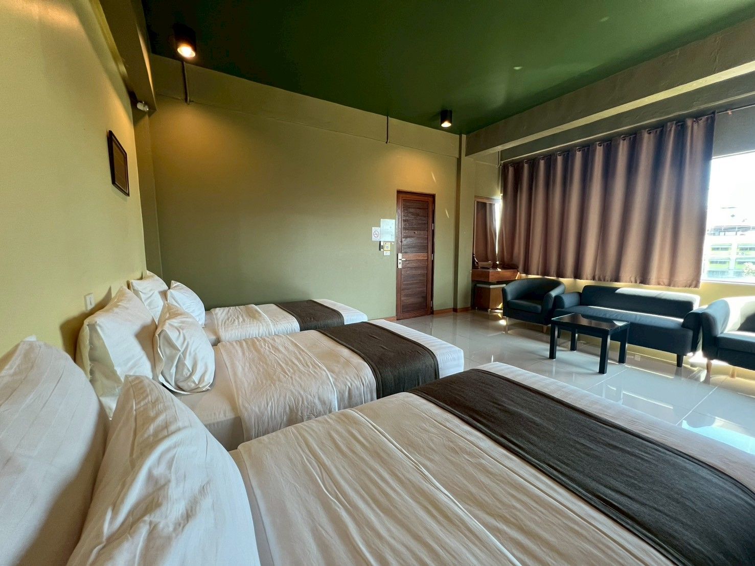 Quarto de hotel com duas camas, um sofá, uma escrivaninha e uma janela com cortinas.