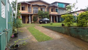A two-story residential building with a front porch, a parked car, and a small garden area. - Hillsview Rest and Guest House (Matale)