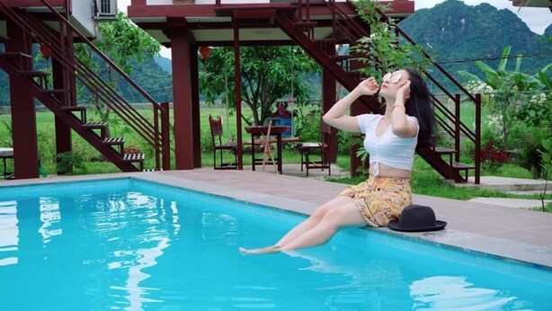 A woman sitting by a pool with a staircase and outdoor furniture in the background. - Hung Phat Bungalow (Phong Nha)