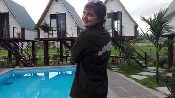 A person standing by a swimming pool with a house in the background.