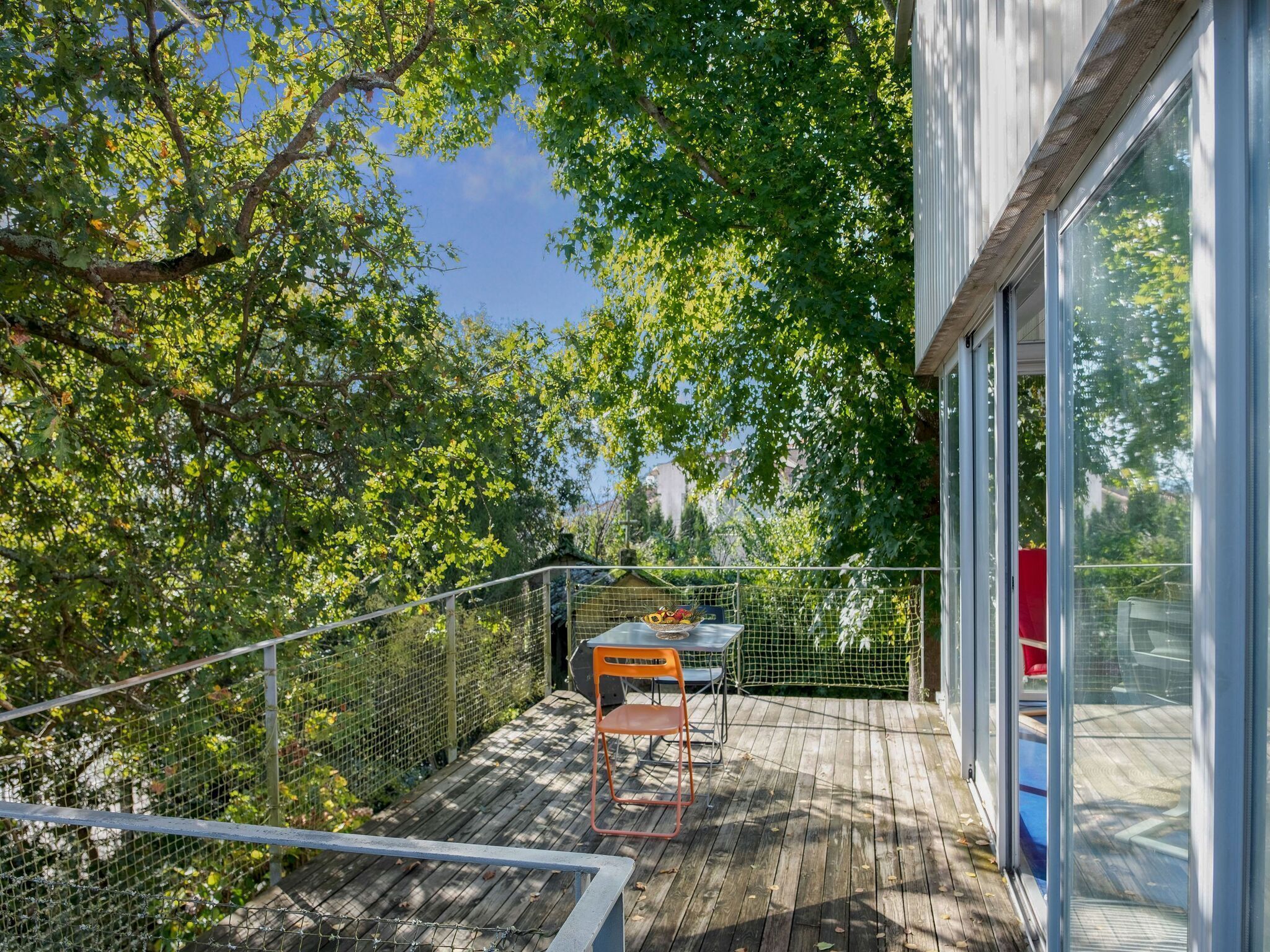 A wooden deck with a table and chairs, surrounded by a metal fence and trees.