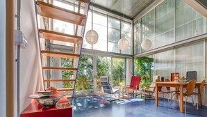 A modern interior with a dining area, a red accent wall, and large windows offering a view of greenery.