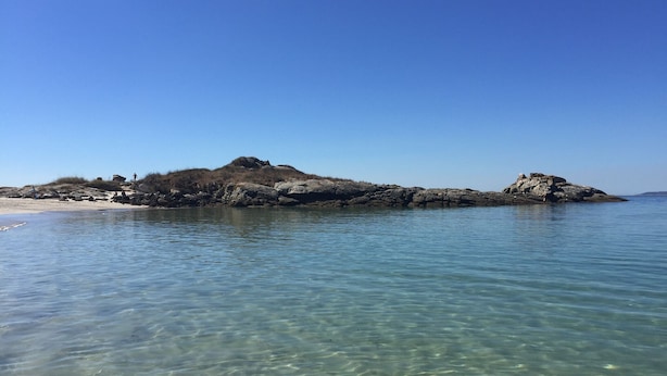 A clear view of a rocky island with a sandy beach in the foreground.