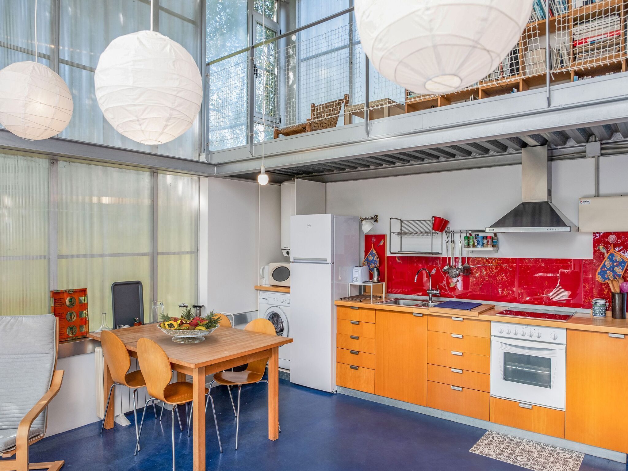 Une cuisine moderne avec un coin repas, caractérisée par un plafond haut, de grandes fenêtres et un pare-feu rouge.