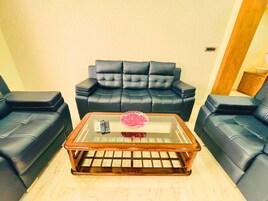 Una sala de estar con una mesa de centro de vidrio, dos sofás de cuero negro y una pequeña mesita de madera.