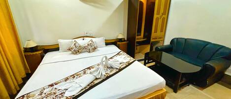 A hotel room with a bed, a desk, a chair, a wardrobe, and a wall-mounted fan.