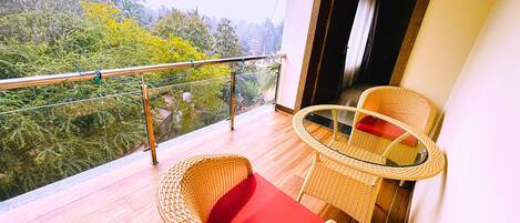 A balcony with wicker furniture, a glass table, and a view of greenery.