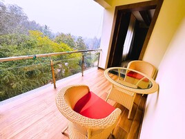 Un balcón con muebles de mimbre, una mesa de vidrio y vista a la vegetación.