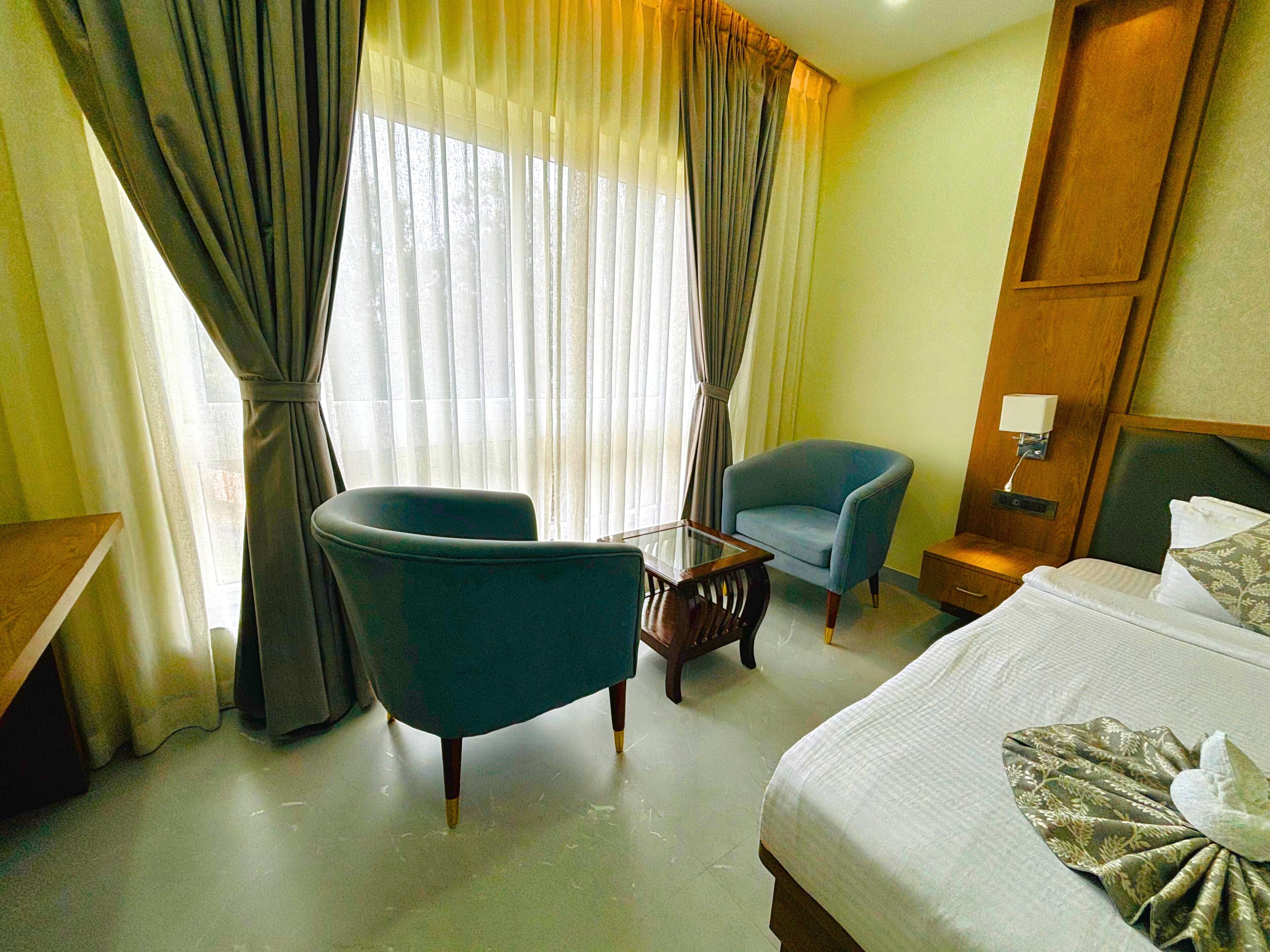 A hotel room with a bed, two armchairs, a small table, and a nightstand with a lamp.