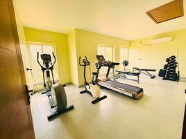 Un gimnasio en casa con equipo de cardio, una banca para pesas y un estante con mancuernas.