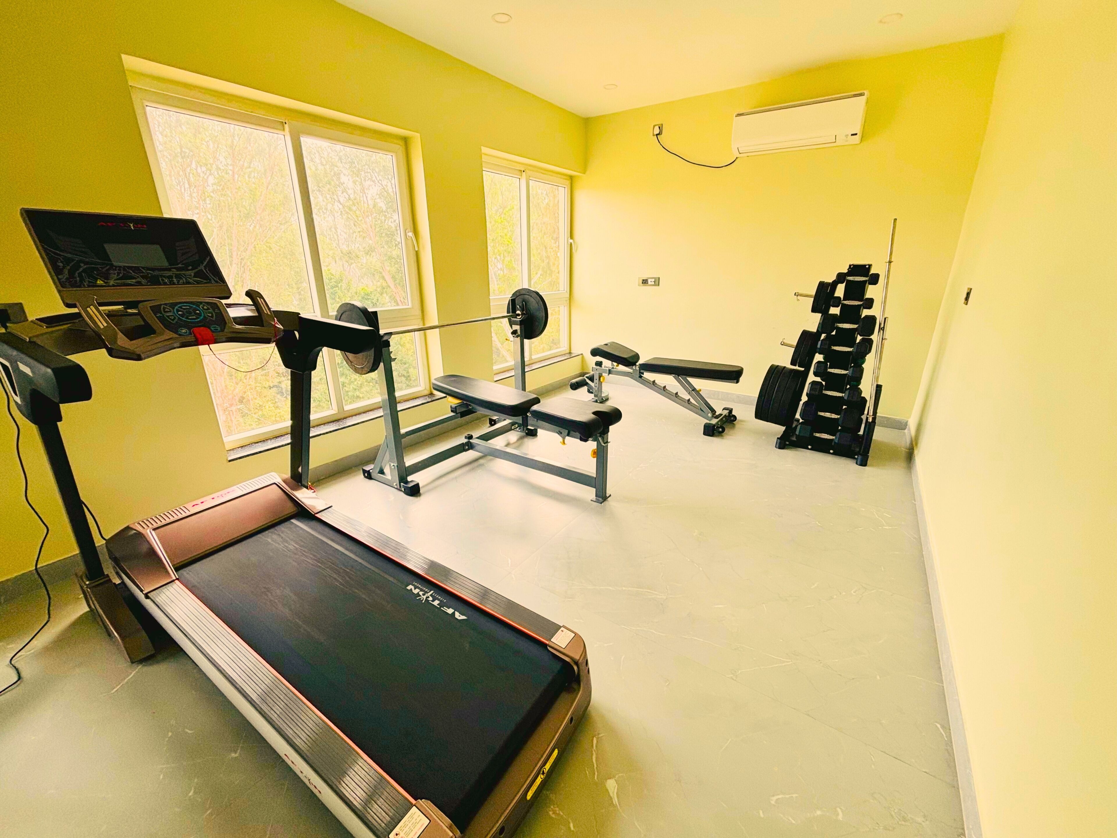 A gym with a treadmill, weight bench, and various free weights.
