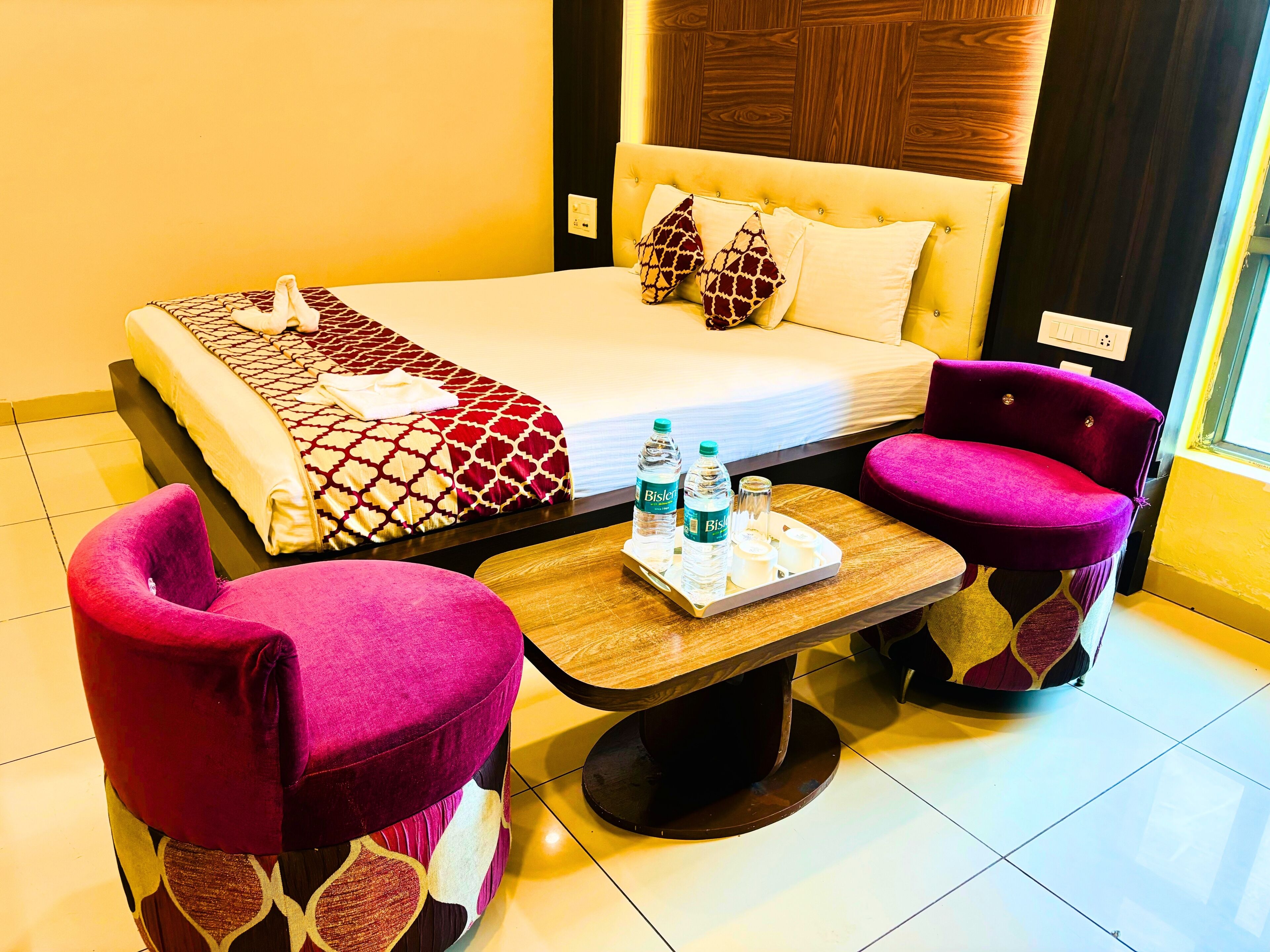 A hotel room with a bed, two armchairs, a small table with water bottles, and a tray.