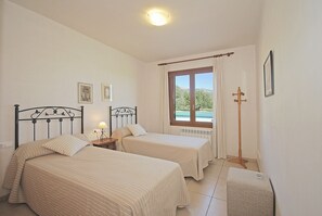 A bedroom with two beds, a window with curtains, a floor lamp, and a radiator.