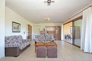 A living room with a sofa, ottoman, and a coffee table. There is a sliding glass door leading to an outdoor area.