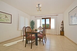 A dining area with a table and chairs, a potted plant, and a view through the window.