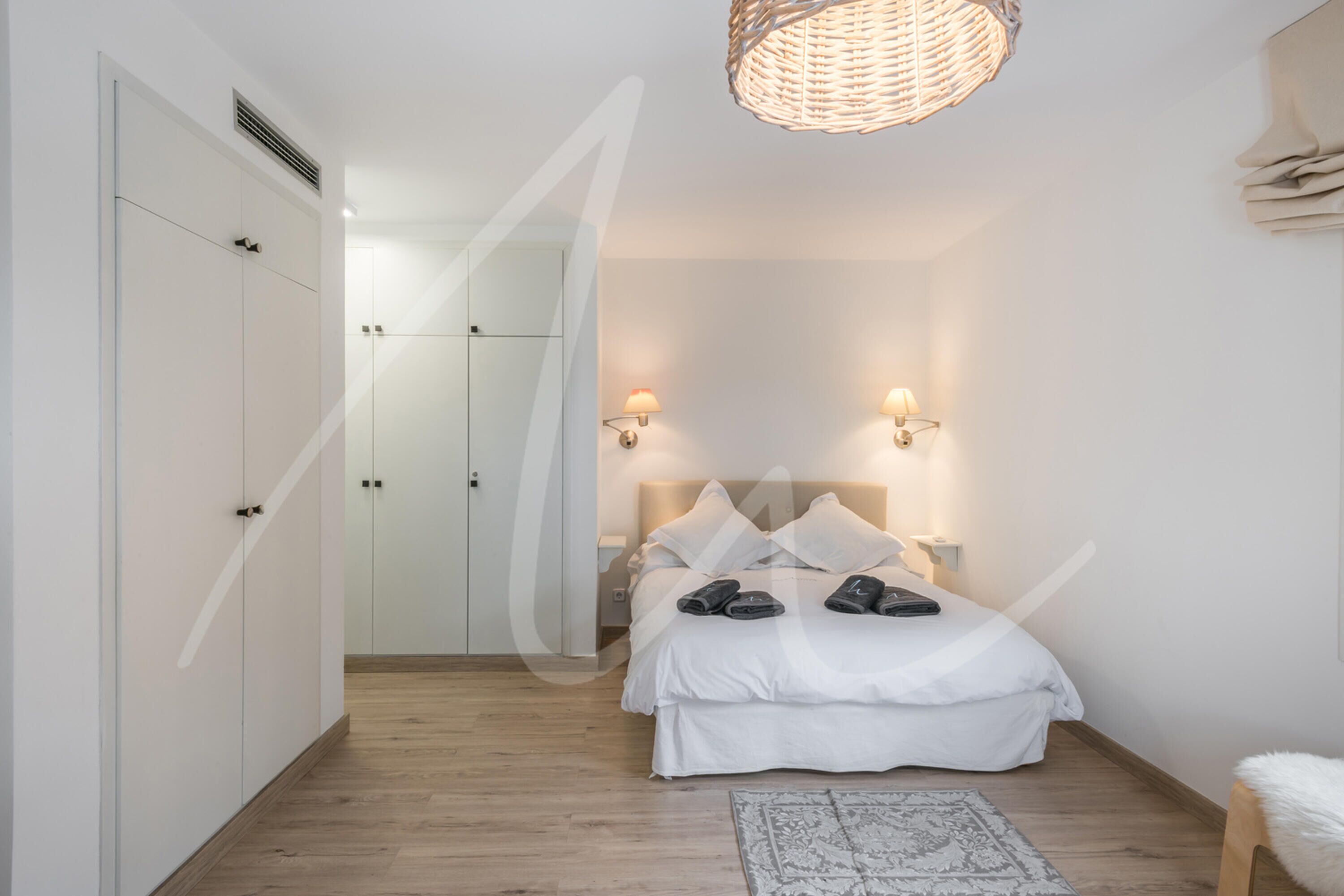 A bedroom with a bed, bedside lamps, a woven light fixture, and a patterned rug.
