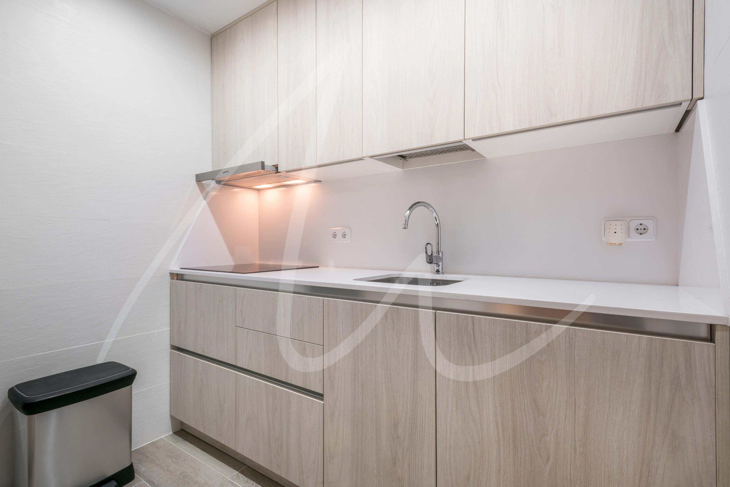 Une cuisine moderne avec des meubles de couleur bois clair, un évier en acier inoxydable et une poubelle noire.