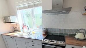 Een keuken met een magnetron, gootsteen, fornuis, oven en een raam met uitzicht op de omgeving.