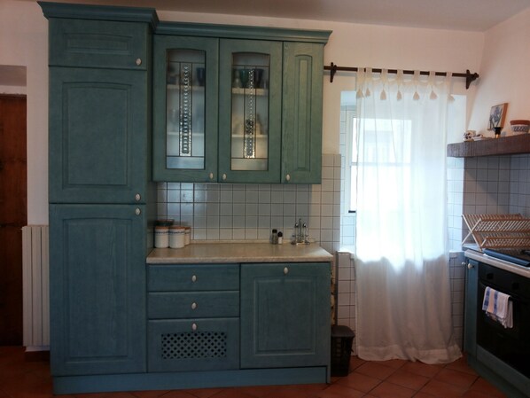 Una cocina con armarios color turquesa, salpicadero de azulejos y una ventana con cortinas translúcidas.