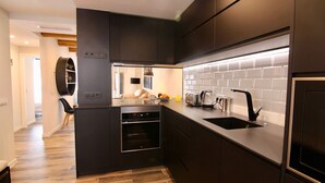 Una cocina moderna con armarios oscuros, horno empotrado, lavamanos y encimera con tetera y frutero.