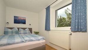 A bedroom with a bed, a window with curtains, a radiator, and a wall-mounted picture. - Cozy cottage with large garden, balcony, veranda  (Reutte)