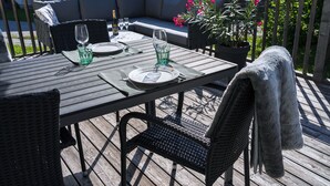 A wooden deck with a table set for two, featuring a woven chair and a cushioned sofa. - Cozy cottage with large garden, balcony, veranda  (Reutte)