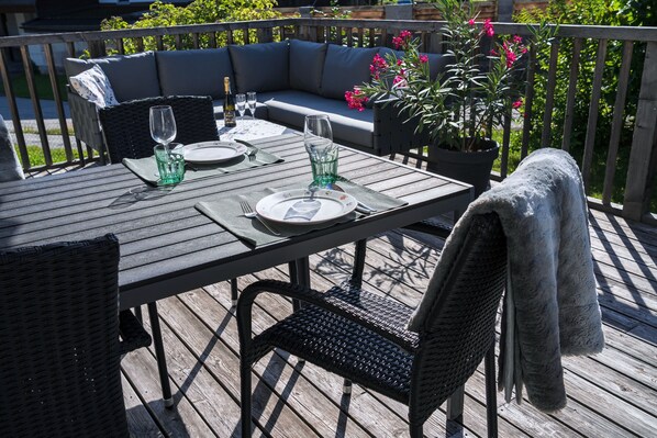 A wooden deck with a table set for two, featuring a woven chair and a cushioned sofa.