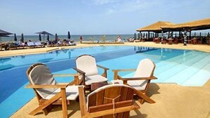 Zona de piscina con sillones de descanso y sombrillas, cielo despejado y vista a la playa.